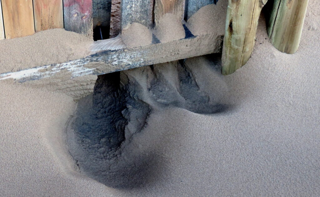 Sand piling up against a wooden fence